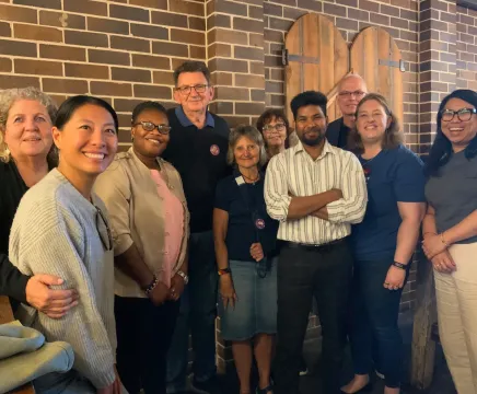 A group past volunteers posing in front of a brick wall at NSW Alumni event.