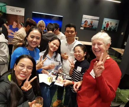 A group of people smiling and posing for a photo at an event with Australian Volunteers Program banner in the background.
