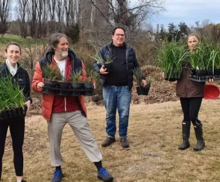 Four people holding plants in their hands. They are standing outside ready to dig the plants into the ground.