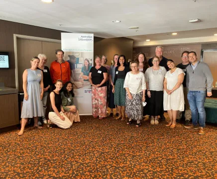 Large group of people standing in a hotel foyer, in front an Australian Volunteers Program banner.