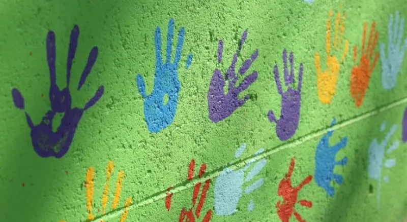 green brick wall with colourful hand prints painted on