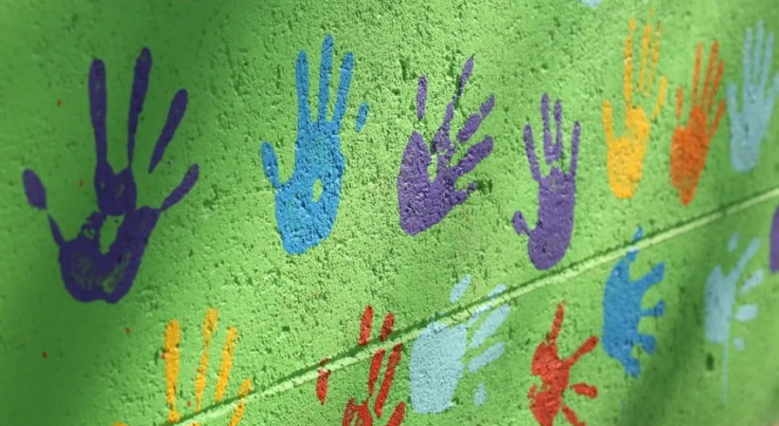 green brick wall with colourful hand prints painted on