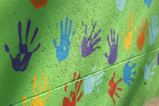 green brick wall with colourful hand prints painted on