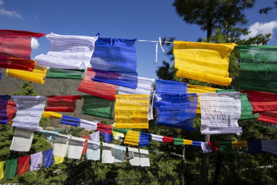 Colourful prayer flags against a backdrop of blue sky and trees.