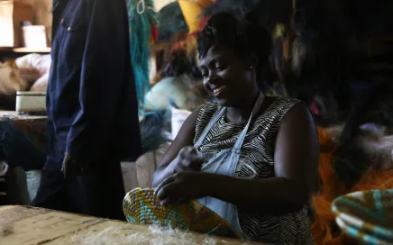 A person weaving with colourful materials and smiling.