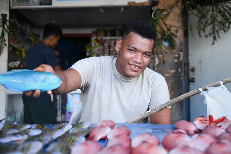 A person at the market in a white t-shirt selling fish at the market.