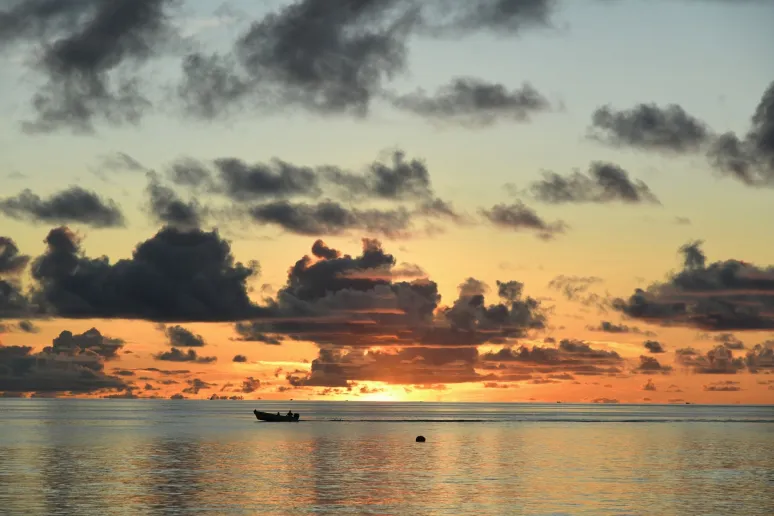 A sunset over the ocean. Clouds in the sky and a boat passing by.