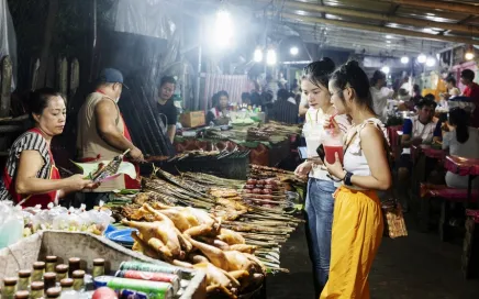 A busy street food market in Laos shows two people shopping for food