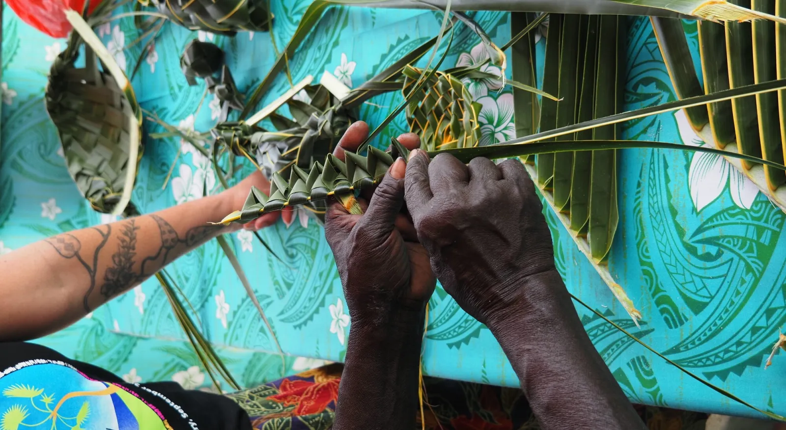 Two hands weaving a creation from plant leaves.