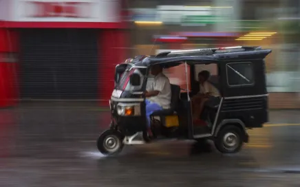 A tuk tuk speeds through a city, the background is a blur