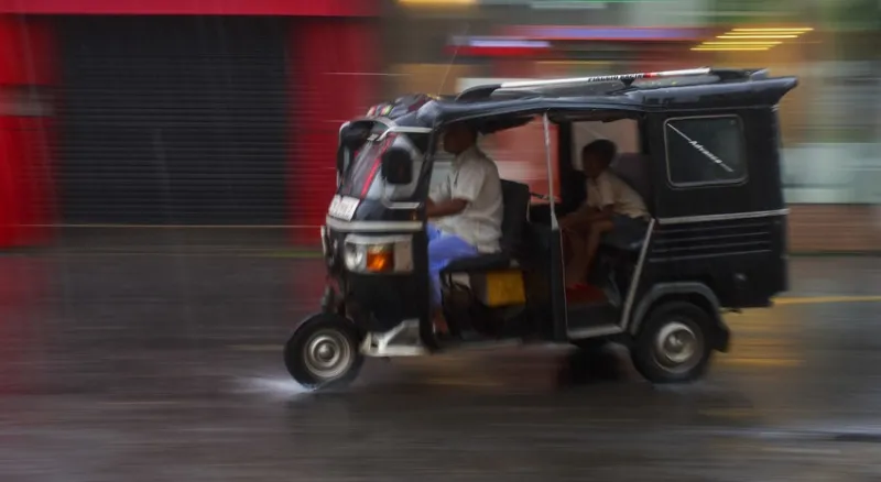 A tuk tuk speeds through a city, the background is a blur