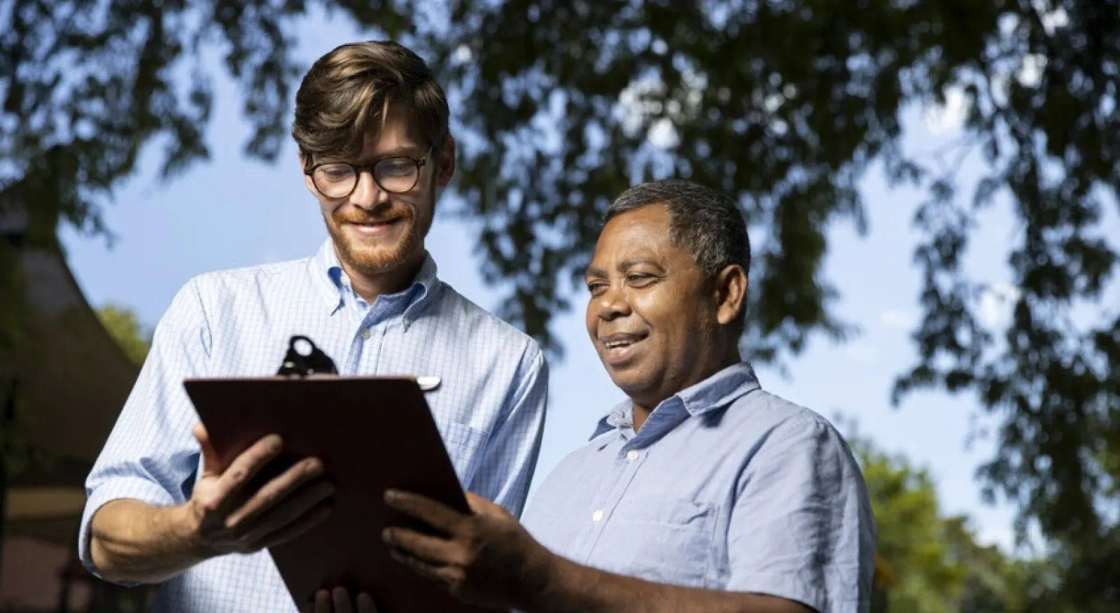 Two people with short-sleeved blue shirts look at a clipboard