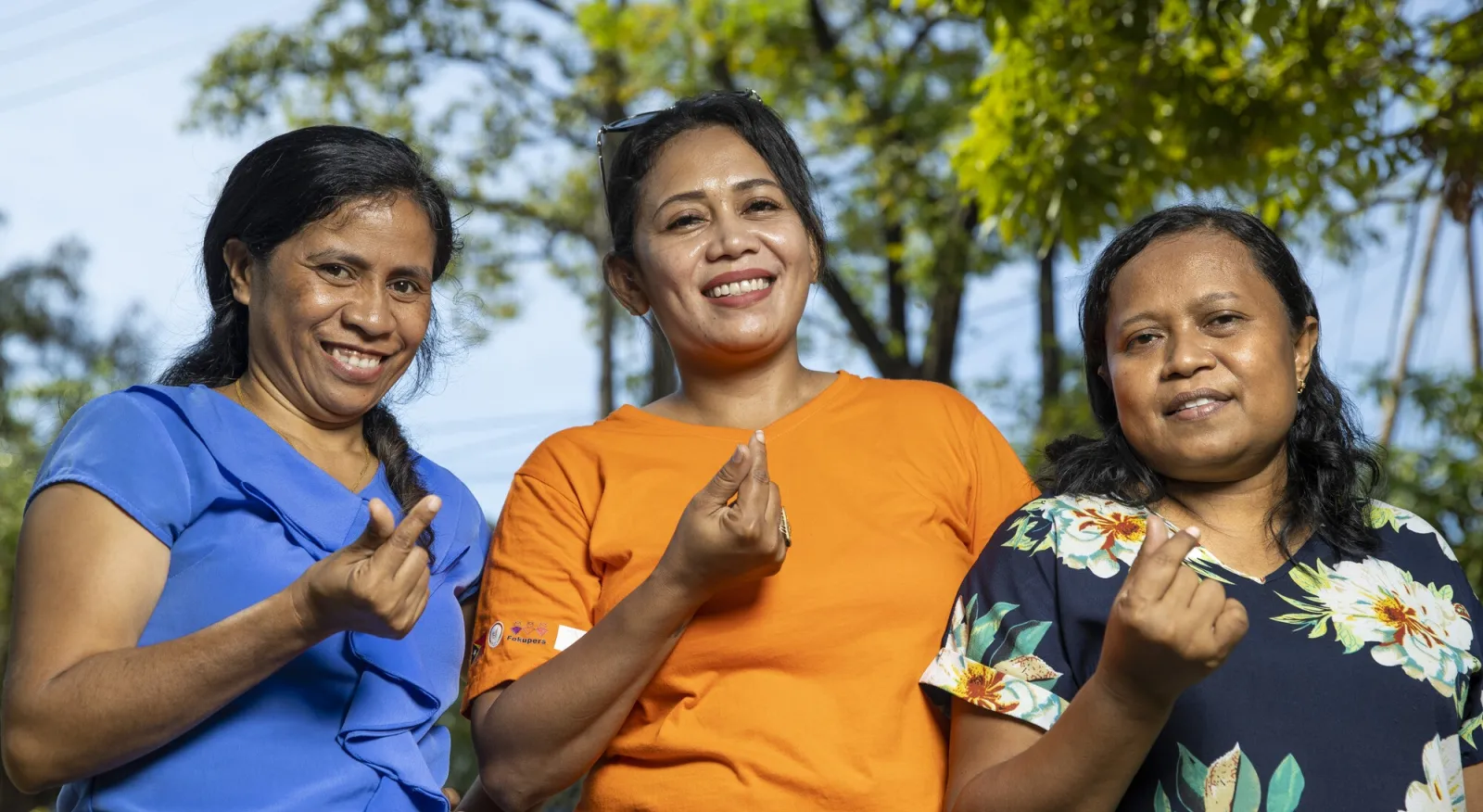 Three women smiling and holding up their fingers to make the symbol for a heart.