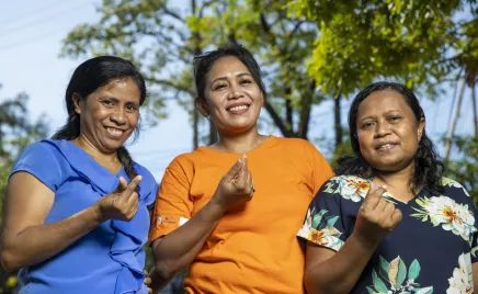 Three women smiling and holding up their fingers to make the symbol for a heart.