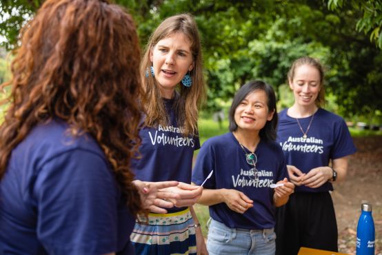 Four women are mid-conversation, all four wear matching Australian Volunteers t-shirts.