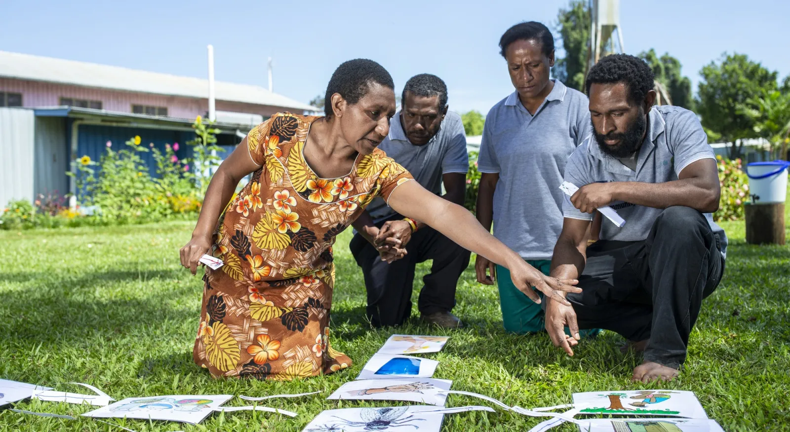 Four people are kneeling on grass, pointing at pieces of paper. They look to be mid-project.