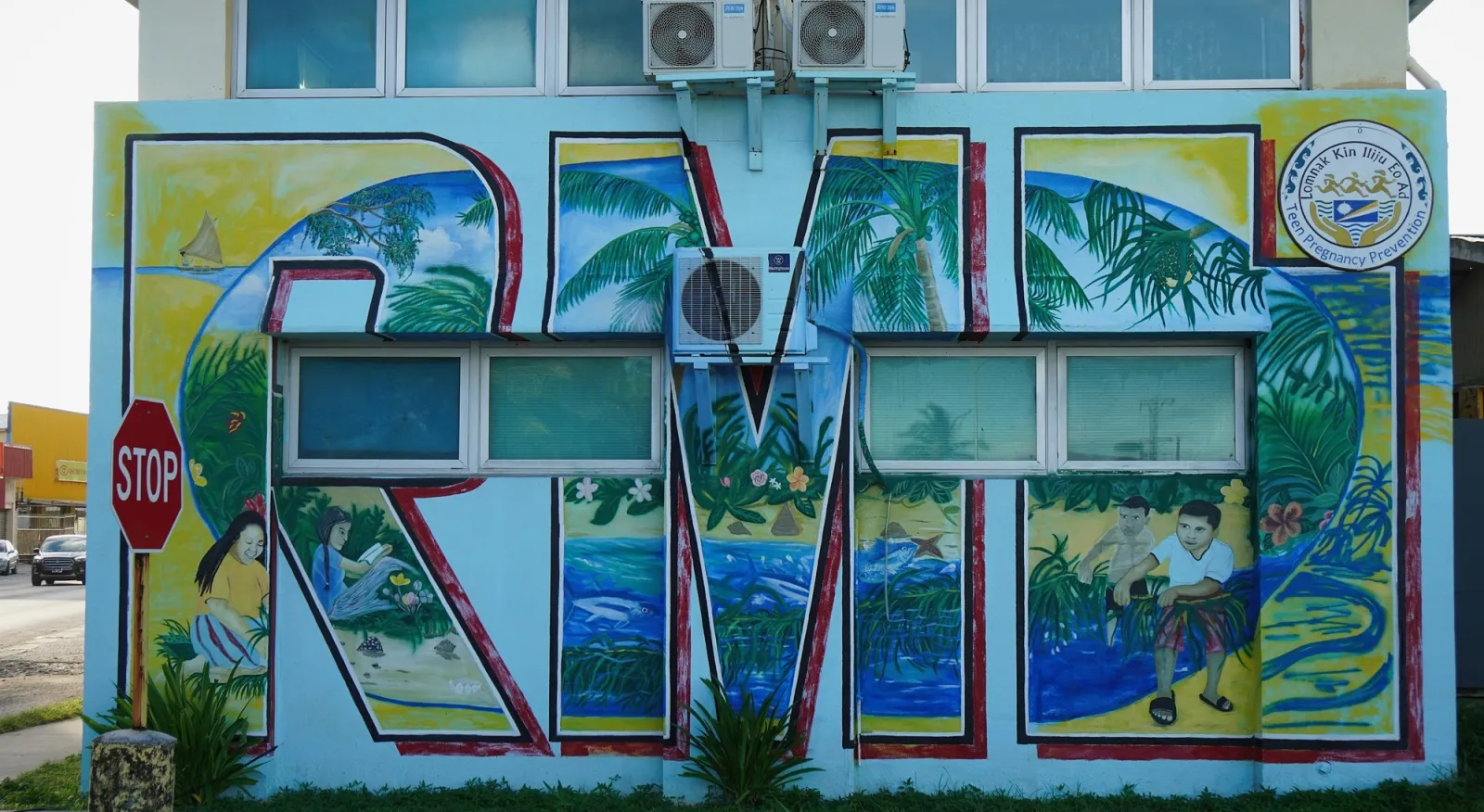 Street art on a building. The letters R-M-I are painted on a wall, the letters are full of palm leaves and surf.