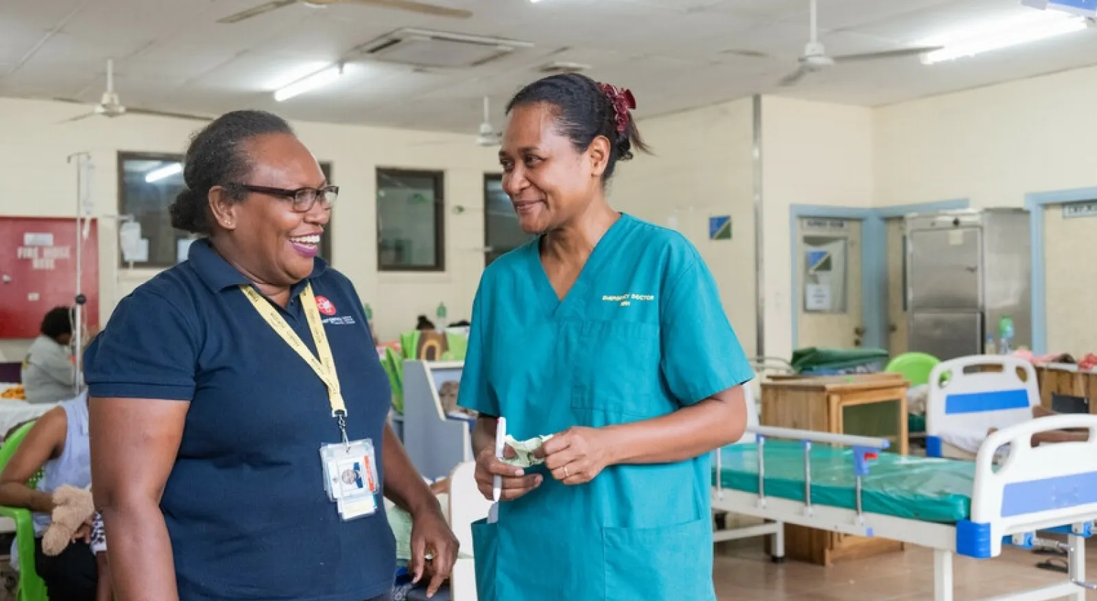 Two medical professionals are standing in a hospital room, facing each other and laughing.