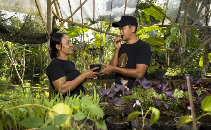 A man and a woman in Emas Hitam's garden in Indonesia. They are surrounded by lush plants, and smiling at each other.