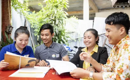 Four people sitting around a table with plenty of papers. They are smiling and in mid-conversation.