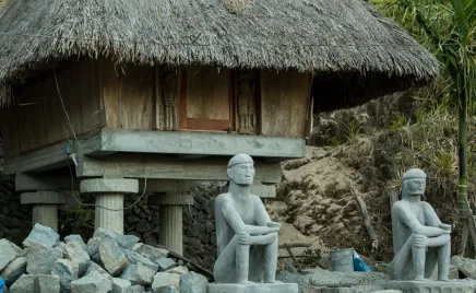 A scenic photo of a beachside building in the Philippines. There are statues of two men sitting outside the door, with rocks built up on either side.