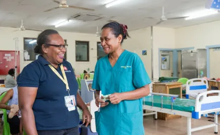 Two medical professionals are standing in a hospital room, facing each other and laughing.