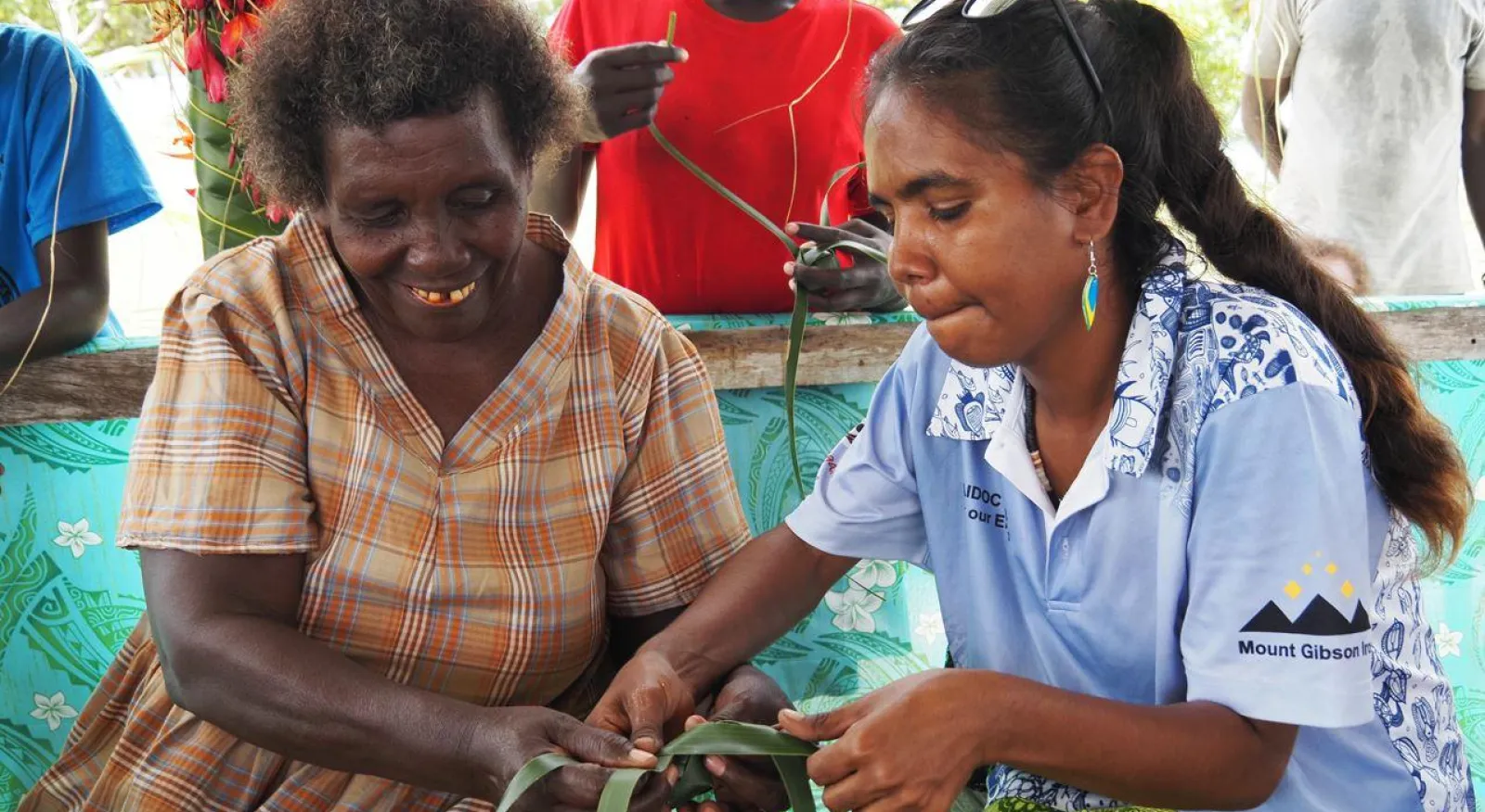 Two people are sitting together, weaving leaves