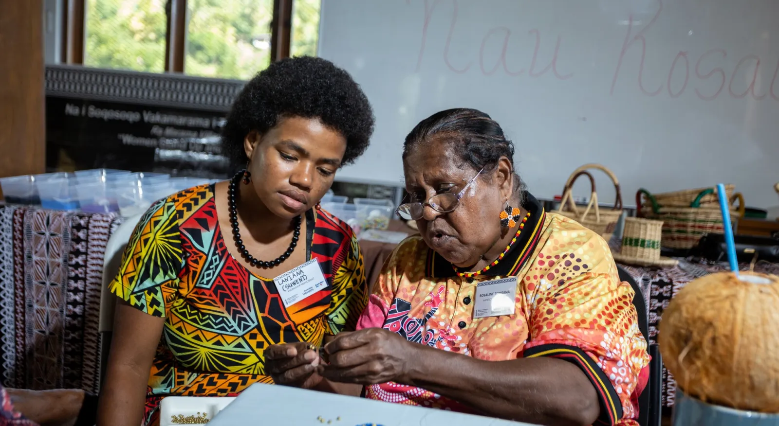 Two people sitting close together looking at some beading.