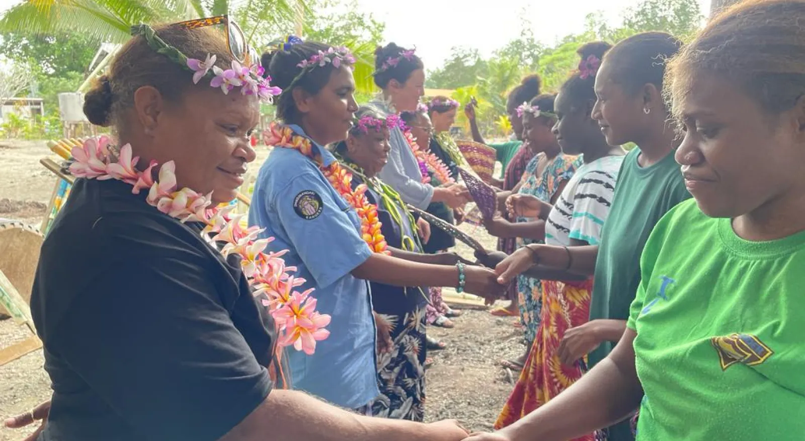 People standing in a line shaking hands, wearing flower wreaths around the necks