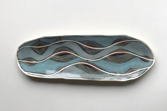 A ceramic plate created by Penny Evans. The background is light blue, with maroon and white lines symbolising a river.