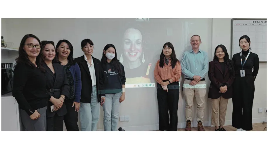 People stand next to a projected screen with a person online