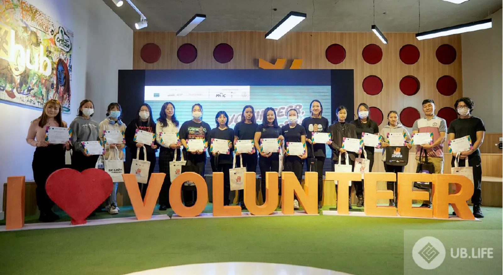A group of individuals standing in front of a sign that reads "I love volunteer."