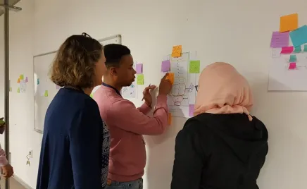 Three people looking at a poster and post-it notes stuck to a wall.