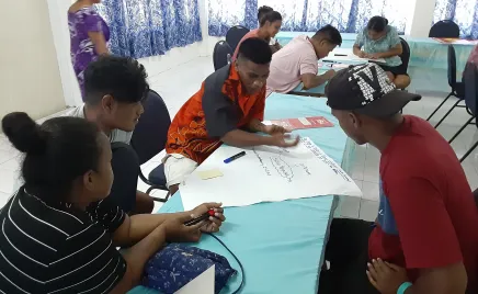 Kiribati youth seated at tables, engrossed in their work with papers spread out before them.