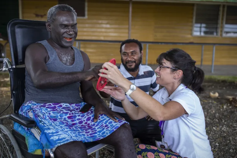 A man and women kindly assists a man in a wheelchair, demonstrating care and support.