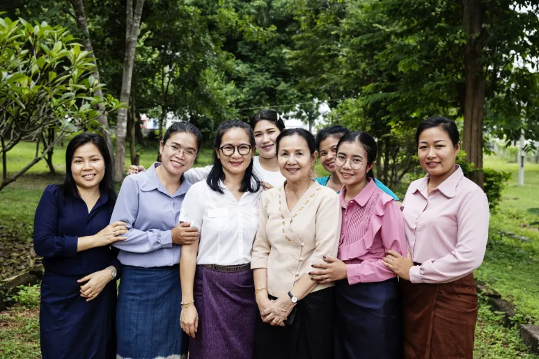 A group of women smiling and posing for a photo in a park, enjoying a sunny day together.