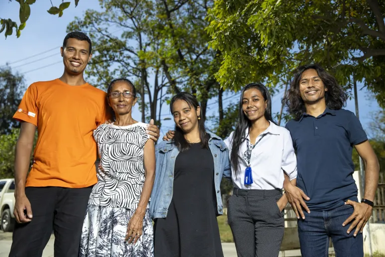 Five people stand outside, smiling at the camera with their arms wrapped around each other.