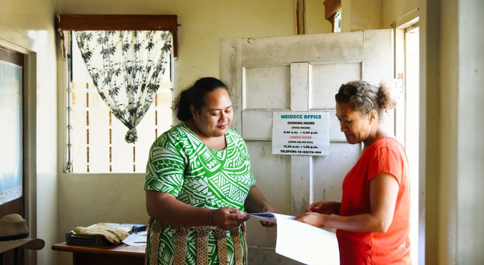 Two women in colourful outfits look over a document together