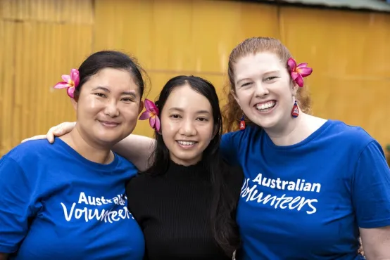 Three women stand shoulder-to-shoulder and smile directly into the camera.