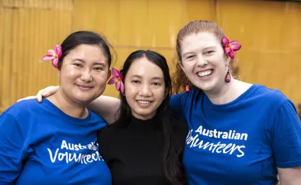 Three women stand shoulder-to-shoulder and smile directly into the camera.