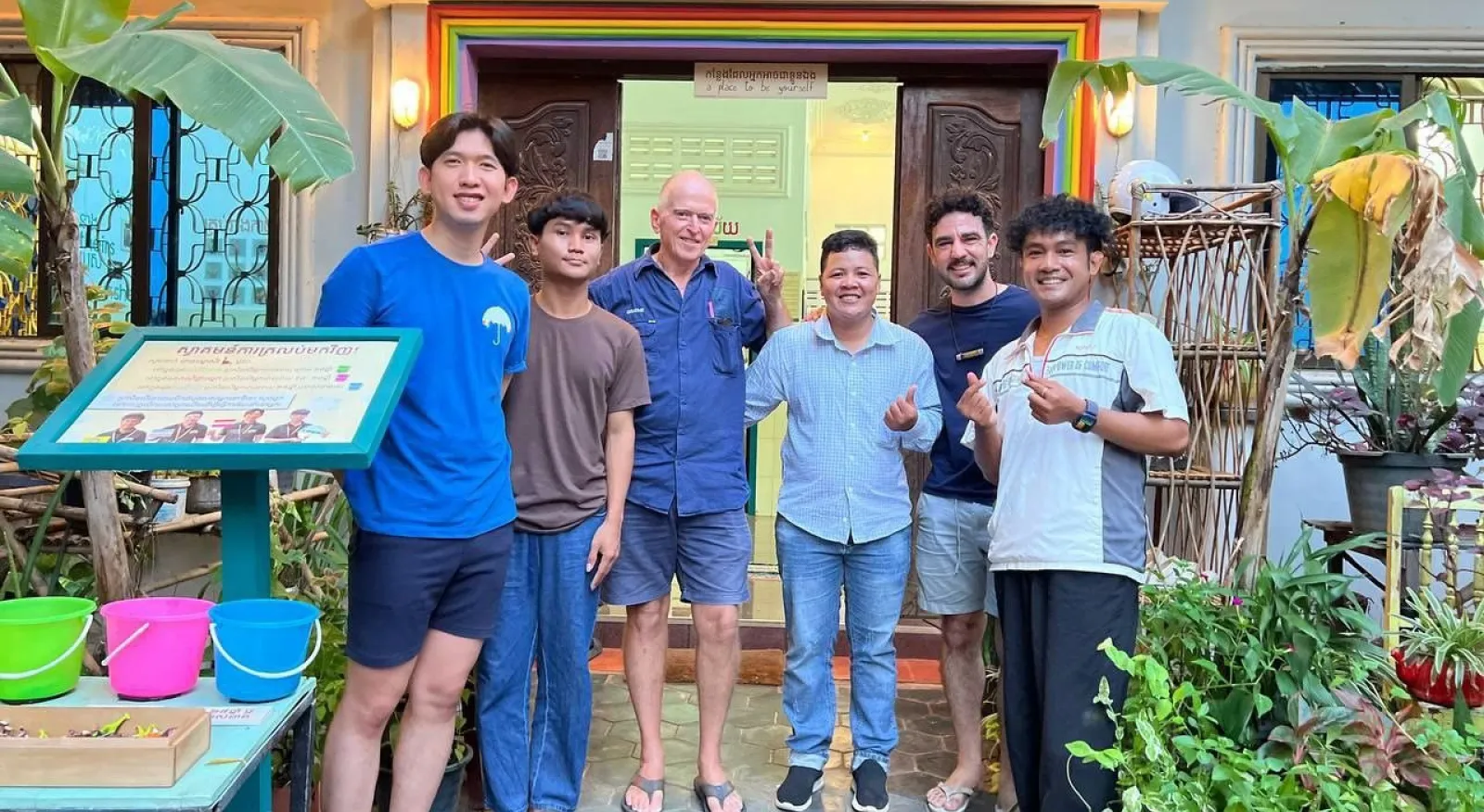 A group of six people standing in front of a brightly coloured building. Everyone is smiling.