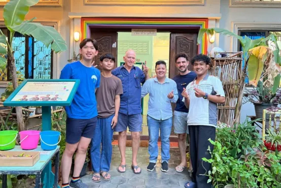 A group of six people standing in front of a brightly coloured building. Everyone is smiling.