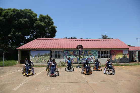 A group of people in wheelchairs on a basketball court, lined up in rows.