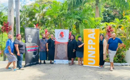 A group of eight people standing in a line outdoors with lush greenery behind them, and three banners reading: 'Stop transphobia'; 'Pacific sexual and gender diversity network'; and 'UNFPA'