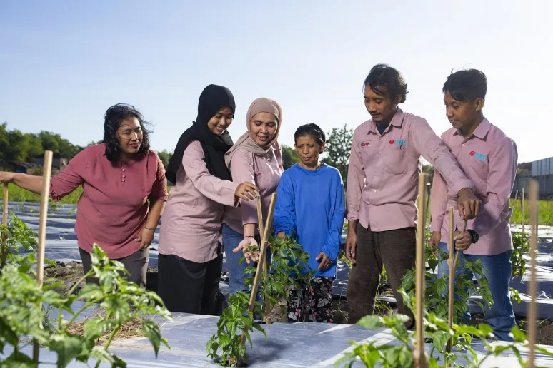 A group of six people standing in a field are all looking towards a plant and smiling. Five of them have pink shirts and the person in the centre has a blue shirt.
