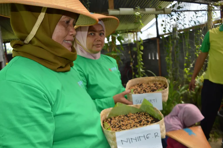 Two women wearing green shirts and traditional hats smiling slightly.