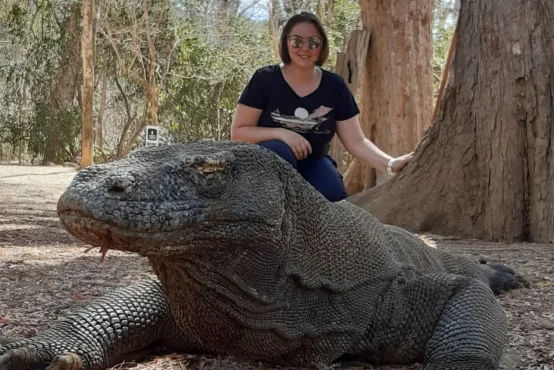A woman stands behind a komodo dragon.