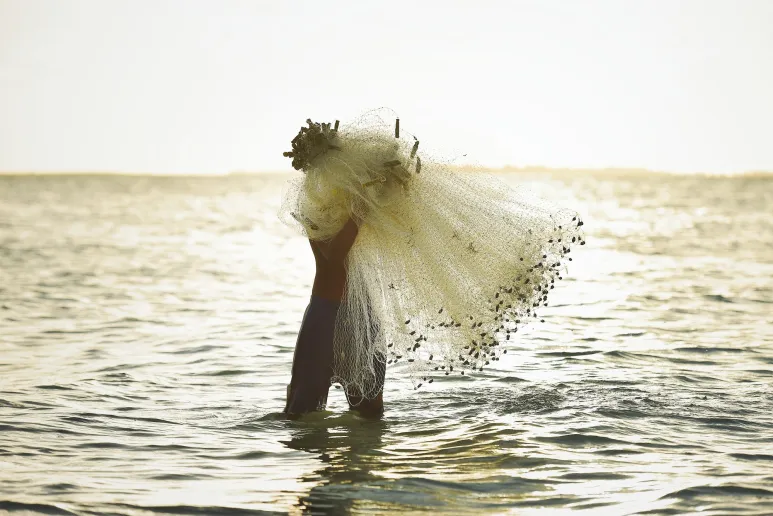 A hand holds up a fishing net out of the ocean.