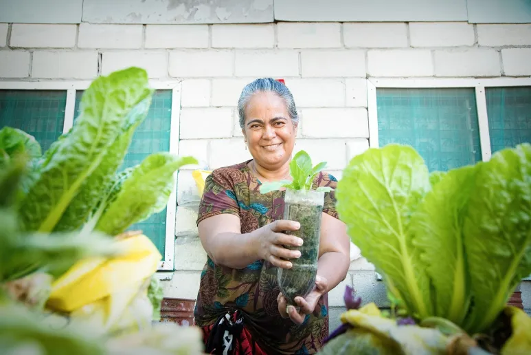 A person holding a small pot made of an old drink bottle, with lettuce growing, and smiling.
