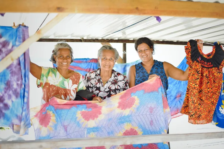 Three people holding up colourful garments and smiling.